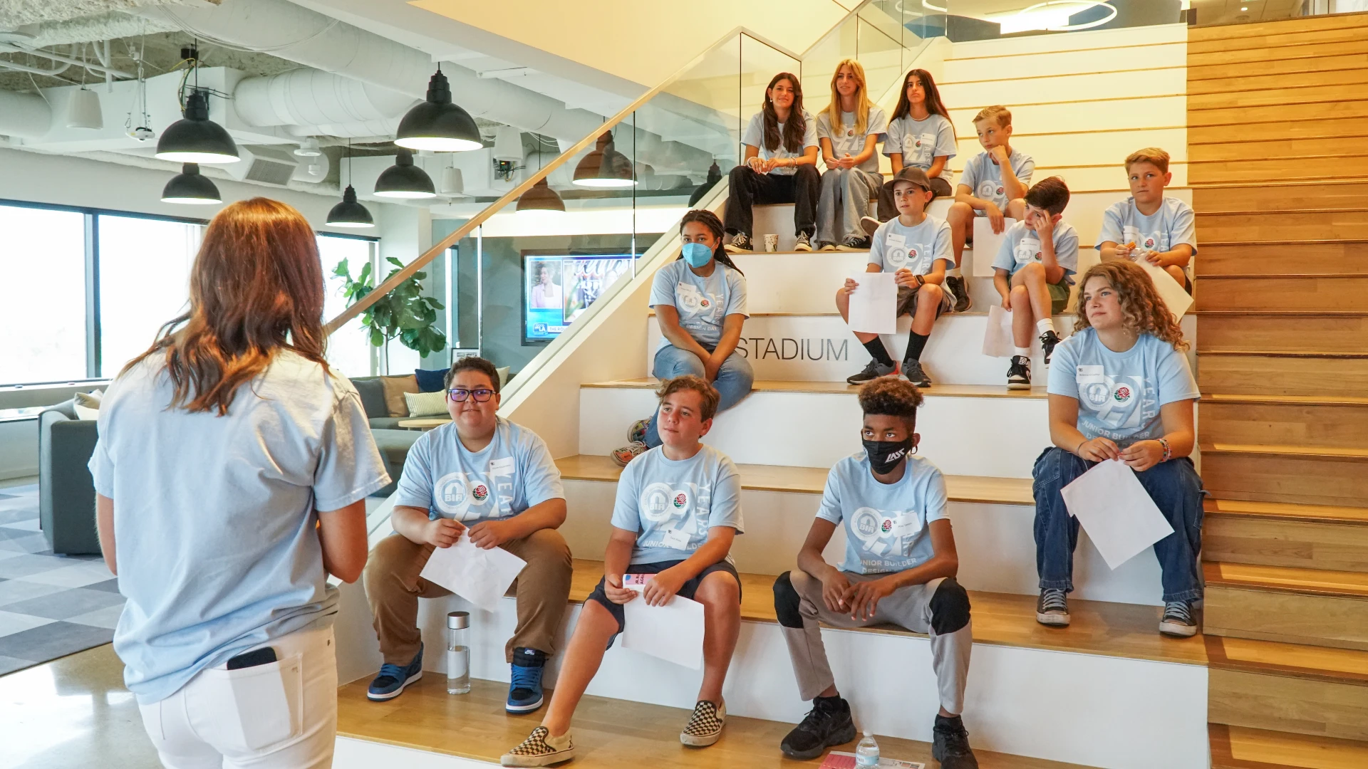 Students participating in the Junior Builder Program, seated on stairs while listening to an instructor.