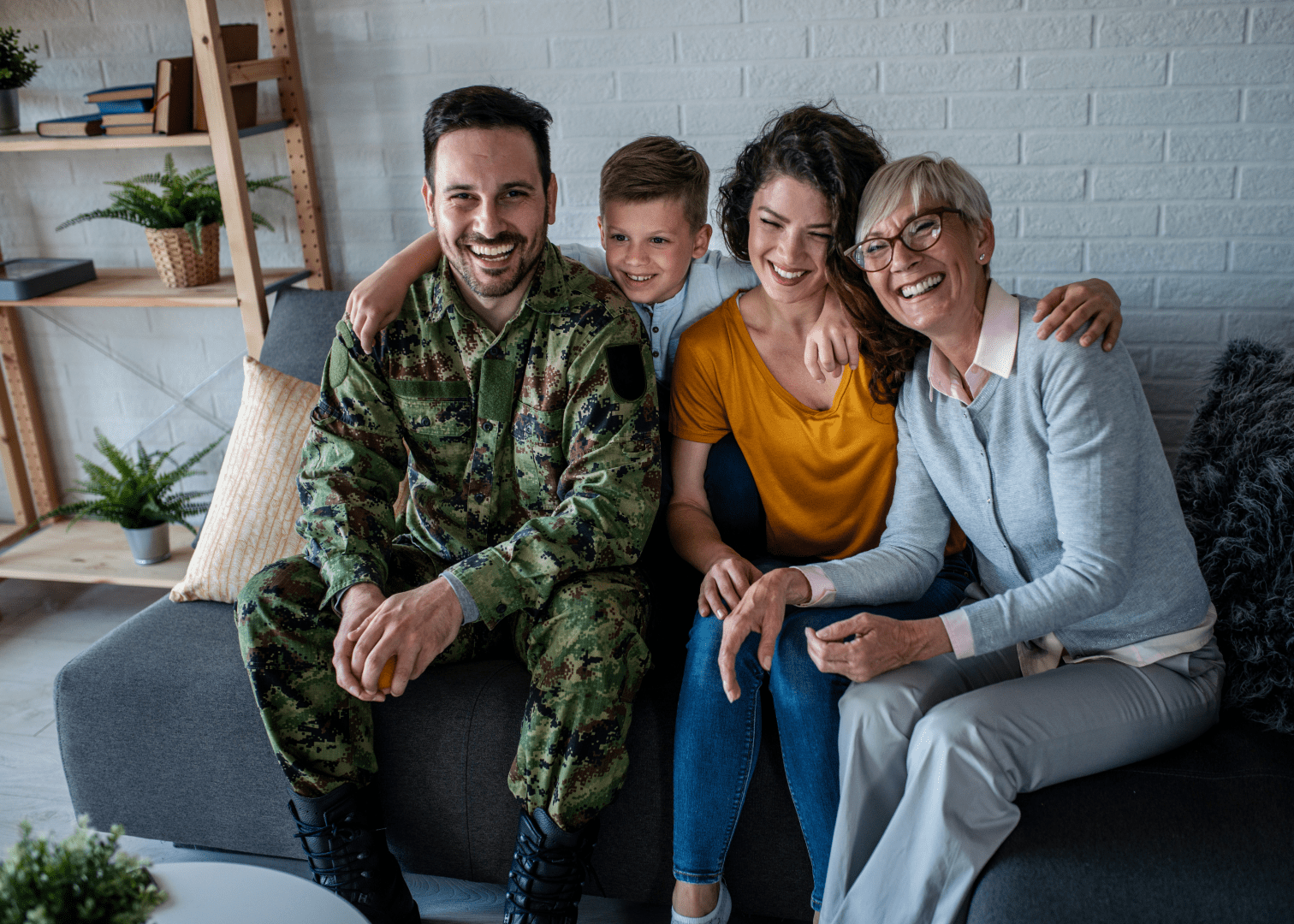 Family of veteran enjoying time together at home A military veteran with his family, including a young boy, woman, and elderly relative, sitting together on a couch.