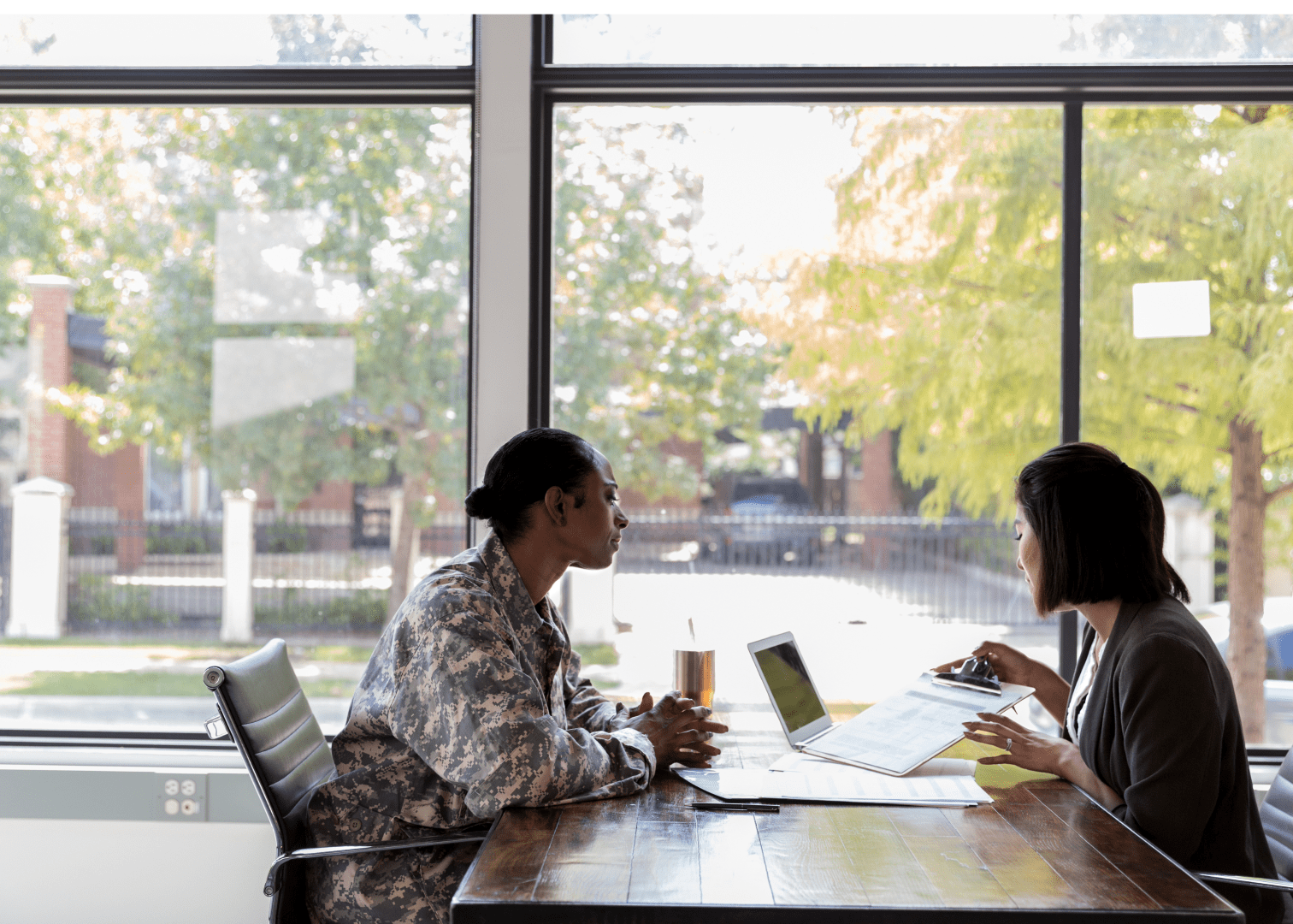 Veteran discussing housing assistance options with a professional A military veteran and a woman sitting at a table in a professional setting, discussing paperwork with a laptop open.