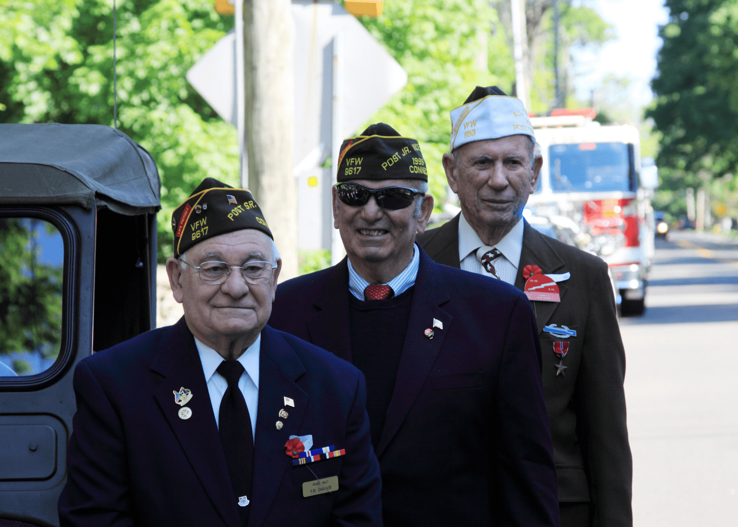 Veterans marching in parade, honoring their service Veterans marching in a parade, wearing VFW hats and military attire, with flags and medals displayed on their uniforms.