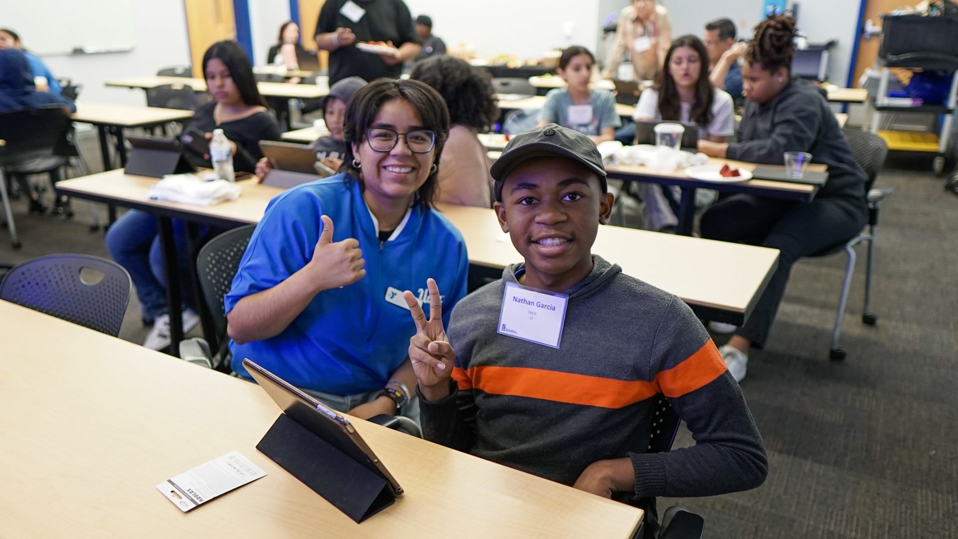 Students at a Junior Builder program, giving thumbs up and peace sign, engaged in home building education.