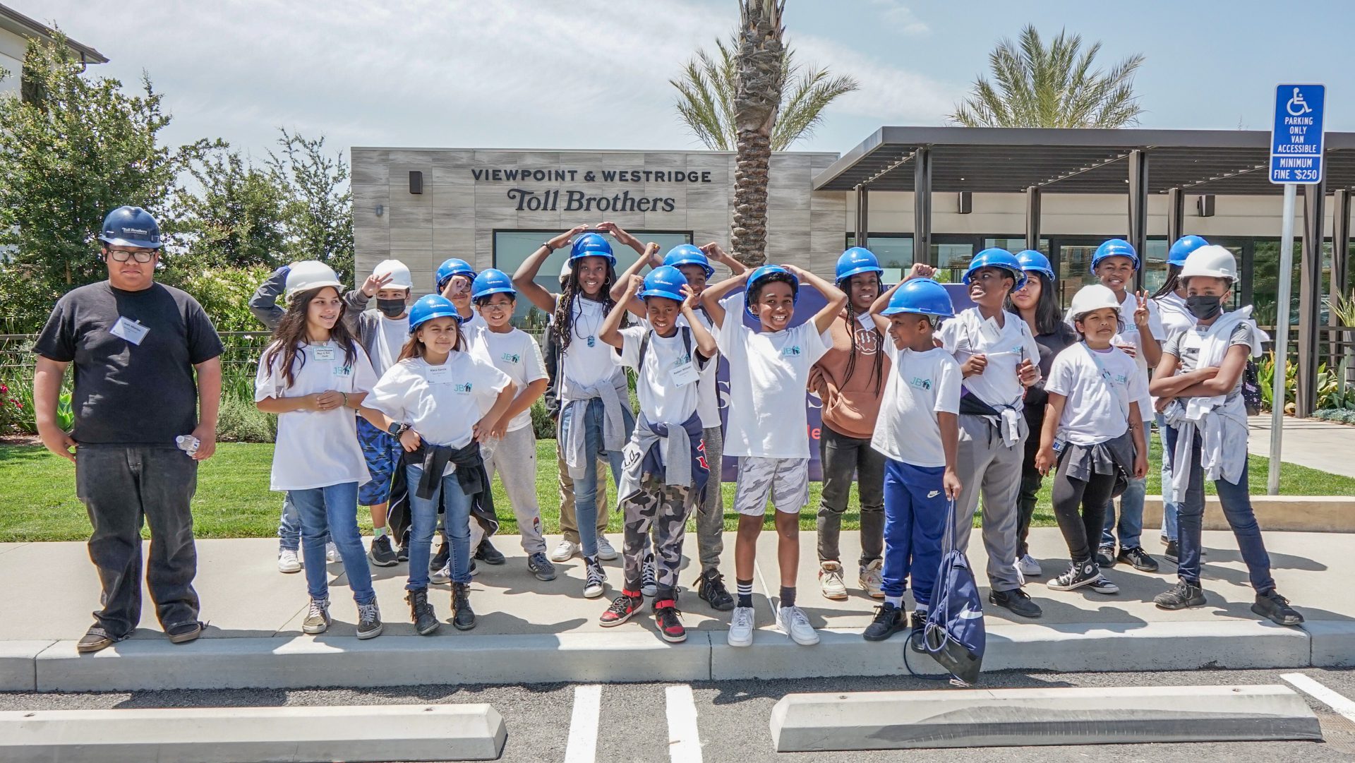 Young participants of the Junior Builder program in hard hats posing in front of the Toll Brothers site sign.